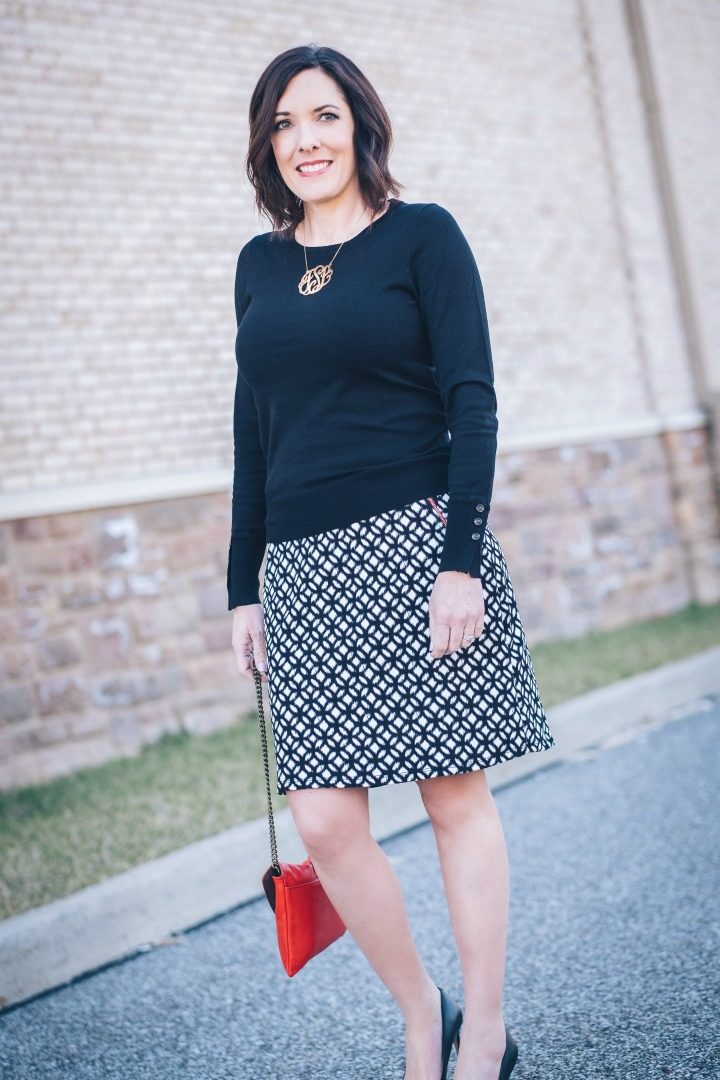 Jo-Lynne Shane wearing an early spring work wear look with LE LIS Maura Zip Pocket Detail Skirt from Stitch Fix with black Sam Edelman Hazel pumps and a red handbag.