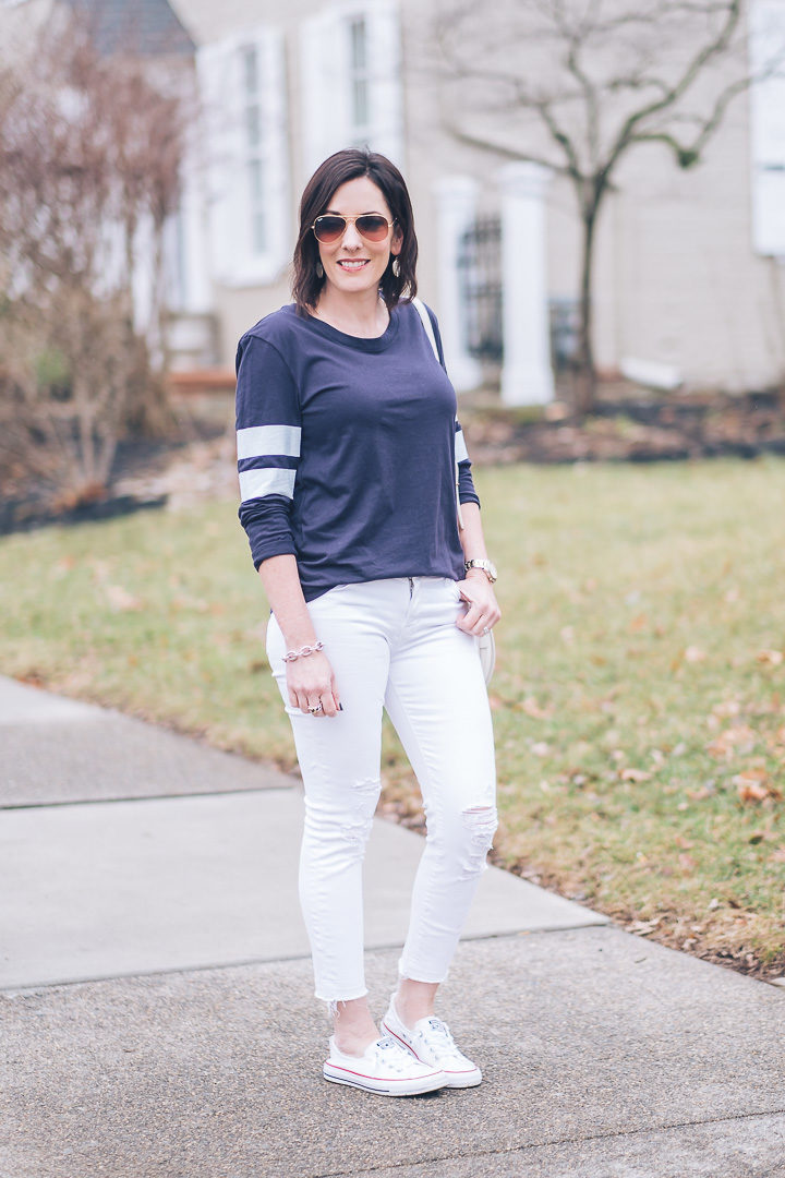 A weekend ready look for spring featuring a navy varsity tee, white distressed cropped jeans, and Converse Shoreline slip-on sneakers.