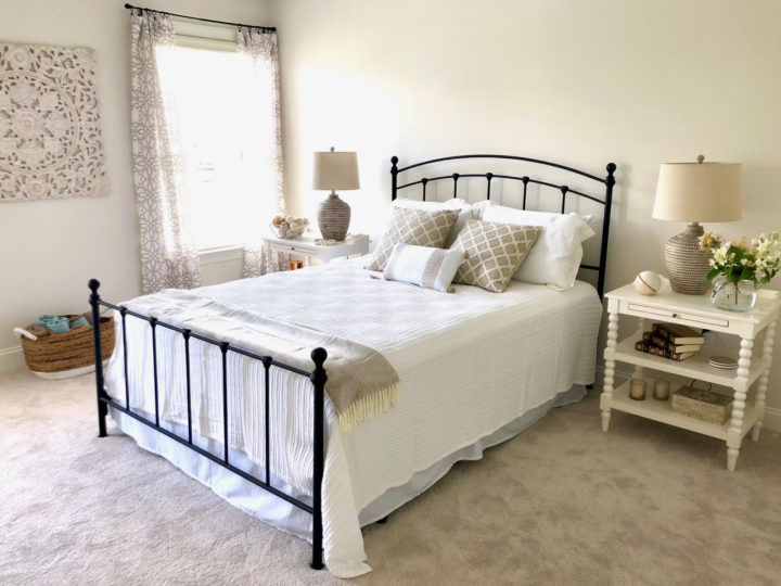 Neutral transitional guest bedroom with black metal panel bed, white mattelasse coverlet, textured geo print window panels, resin table lamps, and white open nightstand.